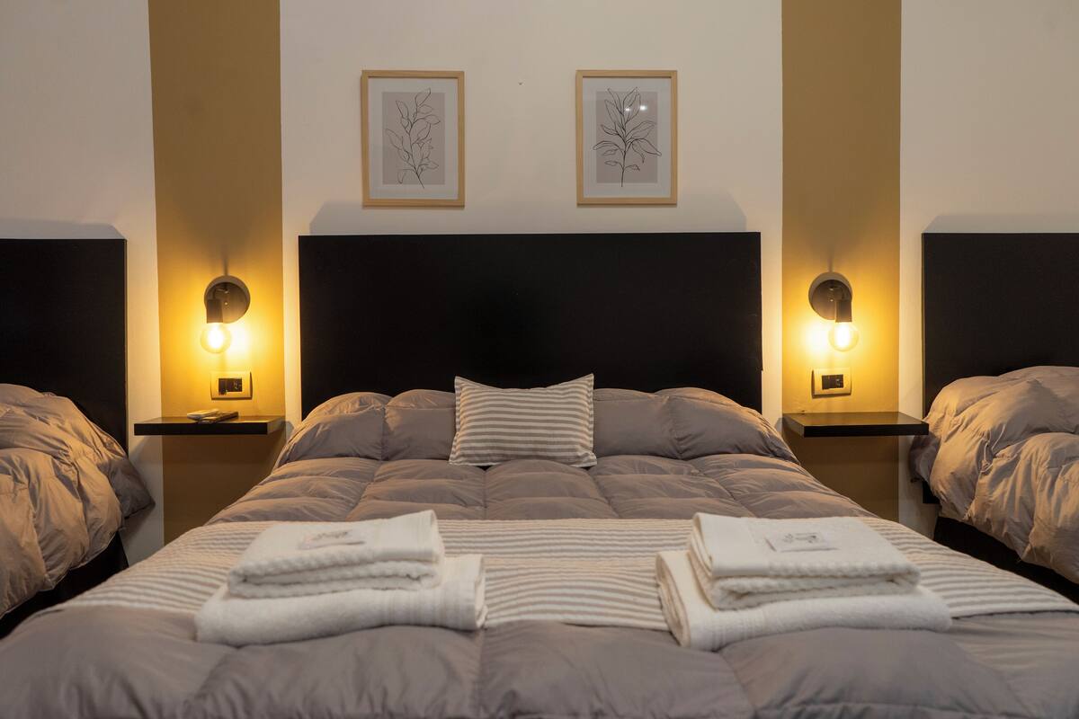A hotel room with a large bed, two bedside tables with lamps, and two framed botanical prints on the wall.
