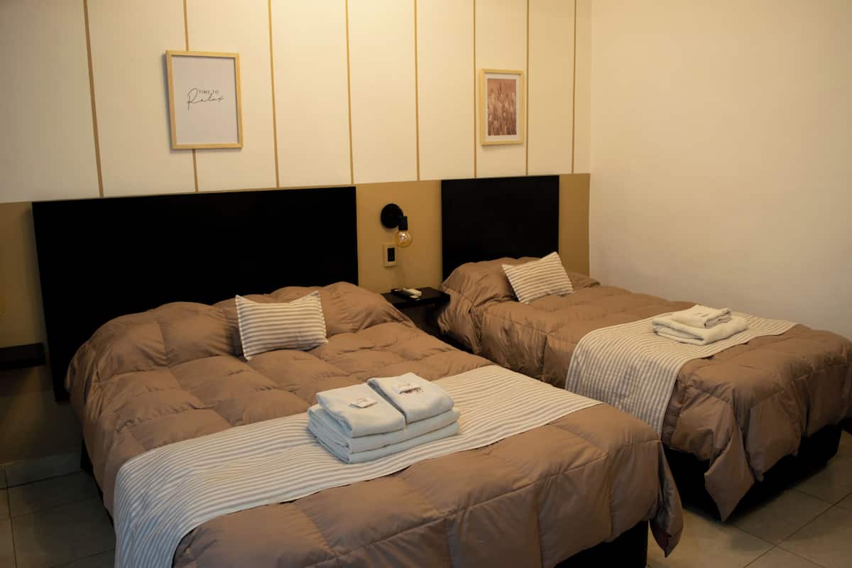 Two single beds with beige bedding, a nightstand, a wall clock, and two framed pictures.