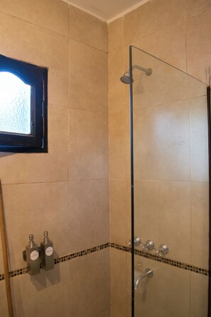 A glass-enclosed shower with a tiled wall, a small window, and a tiled floor with a border. - Hotel del tren  (Salta)