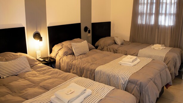 A hotel room with three beds, each with a headboard, a nightstand, and a lamp. - Hotel del tren  (Salta)