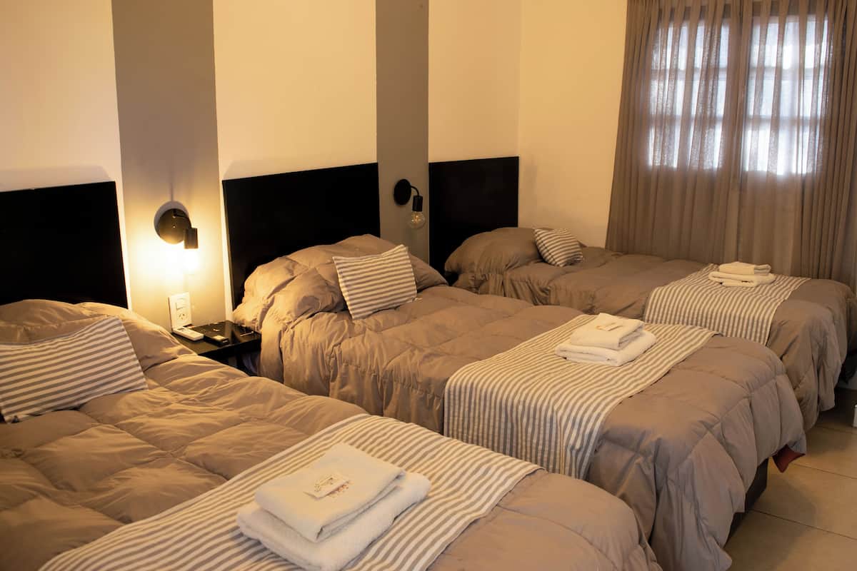 A hotel room with three beds, each with a headboard, a nightstand, and a lamp.