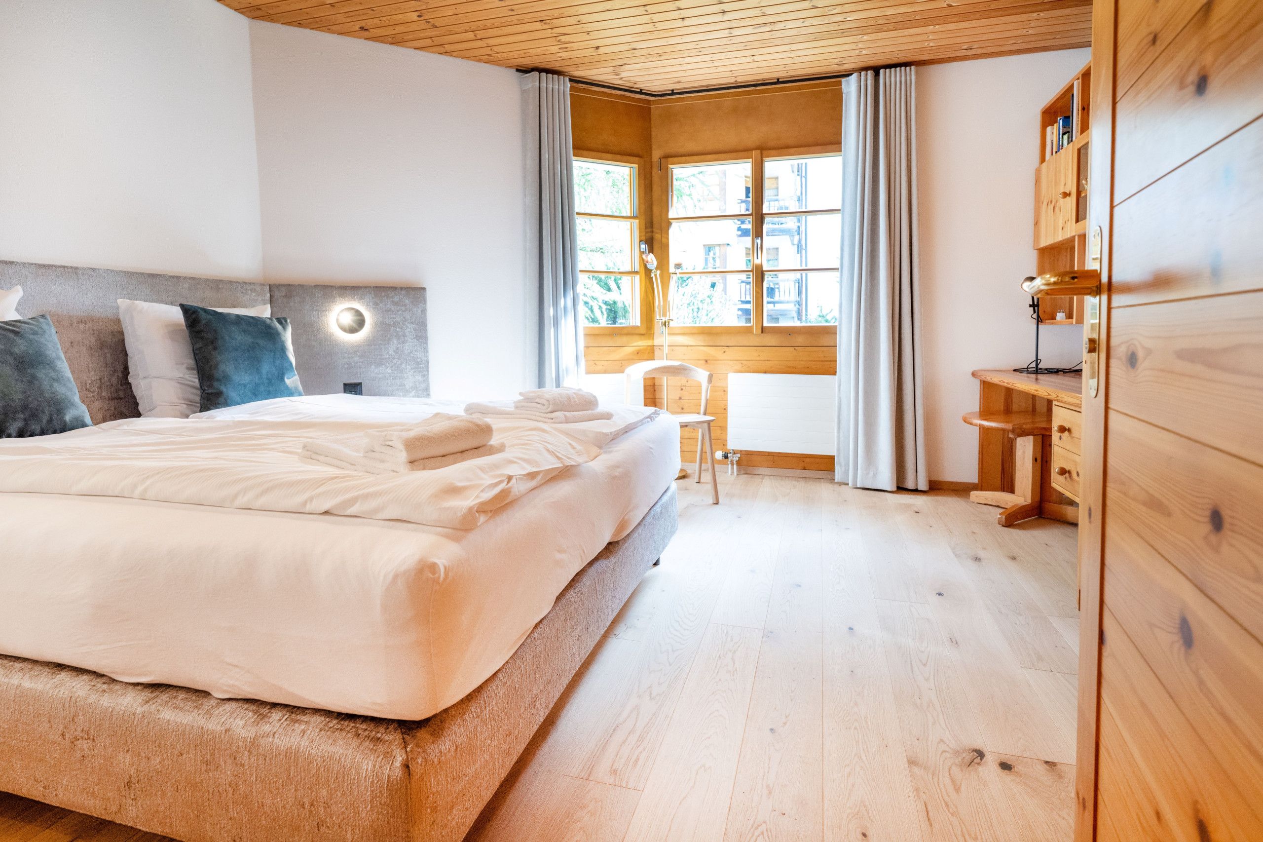 A modern bedroom with a large bed, a wooden wardrobe, and a desk with a chair.