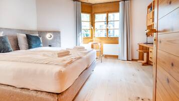 A modern bedroom with a large bed, a wooden wardrobe, and a desk with a chair.