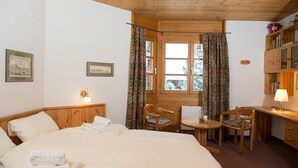 Ein gemütliches Zimmer mit einem Bett, zwei Stühlen, einem kleinen Tisch, einem Schreibtisch und einem Fenster mit Vorhängen.
