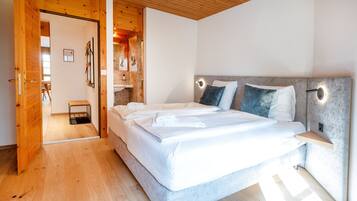 Un dormitorio con techo de madera, una cama grande con ropa blanca, una mesita de noche y un banco empotrado.