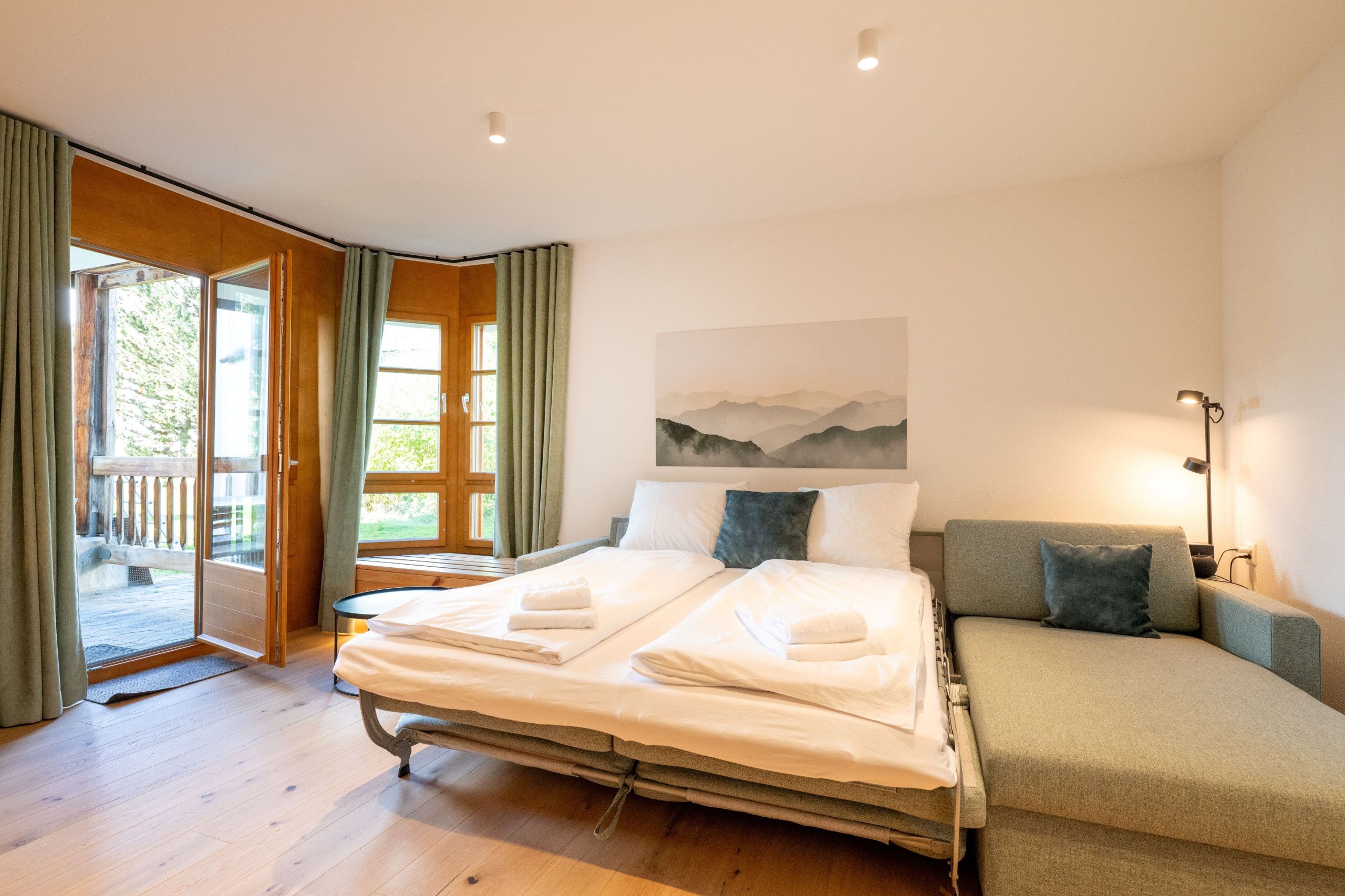 A hotel room with a bed, a sofa, a painting, and a view of the outdoors.