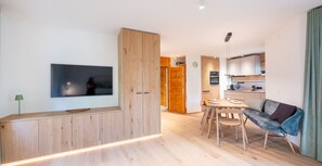 A modern living space with a wooden cabinet, a TV, a dining area with a table and chairs, and a sofa.