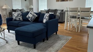 A living room with a sectional sofa, a dining table with chairs, and a kitchen area. - POOL, 5 min walk to Jenks, 4 Bedroom, 4 car parking, beach badges, Fence, Pets (Point Pleasant Beach)