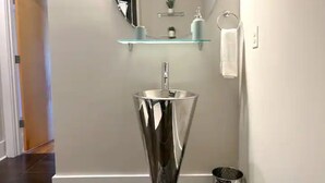 Ein Badezimmer mit einem modernen Waschbecken, einem Spiegel und einer Glasablage darüber.