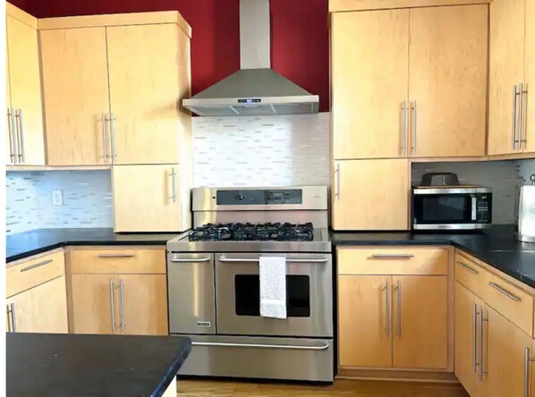 Kitchen equipped with a gas stove, oven, and microwave, along with light wood cabinets and a black countertop.