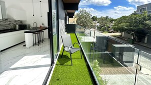 Una cocina moderna con una isla grande, un comedor con barandilla de vidrio que da a un césped verde y una vista despejada del vecindario.
