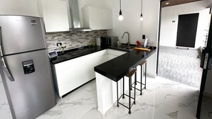 Una cocina moderna con refrigerador de acero inoxidable, armarios blancos, encimera negra y piso de mármol.