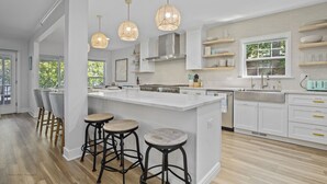 Cozinha moderna com uma ilha grande, banquetas, luminárias pendentes e armários brancos.