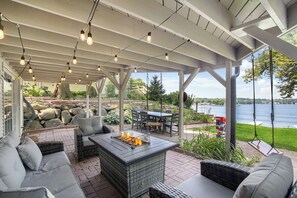 A covered patio with outdoor furniture, a fire pit, and a view of a lake. - Lakefront Oasis w/ 2 fire pits, game room & kayaks (Fox Lake)