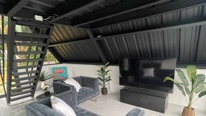 Un salon moderne avec un canapé gris, un téléviseur à écran plat et un escalier menant à un niveau supérieur.