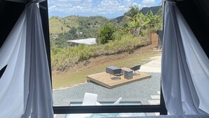 Une chambre avec une grande fenêtre, un lit et une vue sur un jardin et des collines.