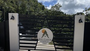 Une entrée fermée par un portail, sur laquelle est apposée une plaque indiquant : « Kei Cabin, une qualité de vie supérieure depuis 2022 ».