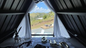 Une pièce chaleureuse et faiblement éclairée, avec un lit, une petite table et une fenêtre donnant sur un paysage verdoyant.
