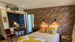 A bedroom with a large bed, a desk, a chair, and a window with curtains.