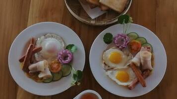 Dos platos de comida con huevos, verduras y carne, además de una cesta de tostadas sobre una mesa de madera.