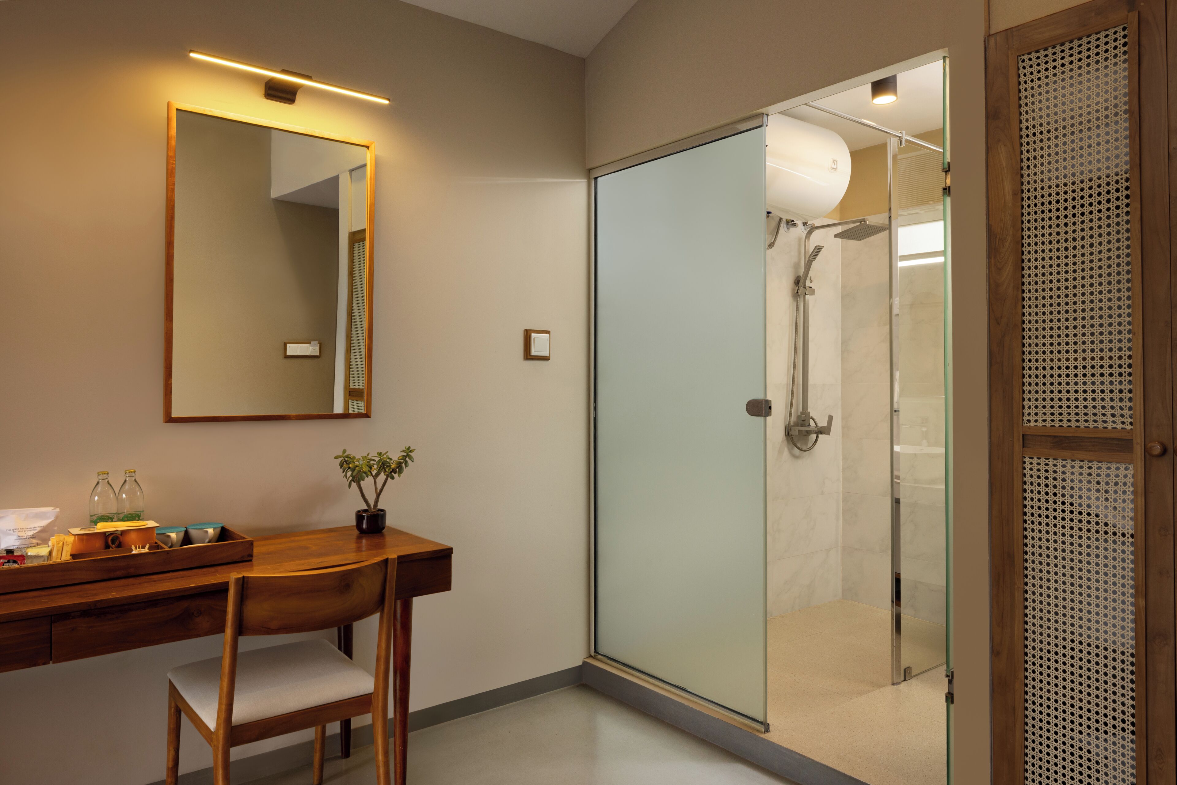 A modern bathroom with a wooden desk, a mirror, a potted plant, and a glass-enclosed shower area.