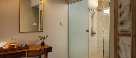 A modern bathroom with a wooden desk, a mirror, a potted plant, and a glass-enclosed shower area.
