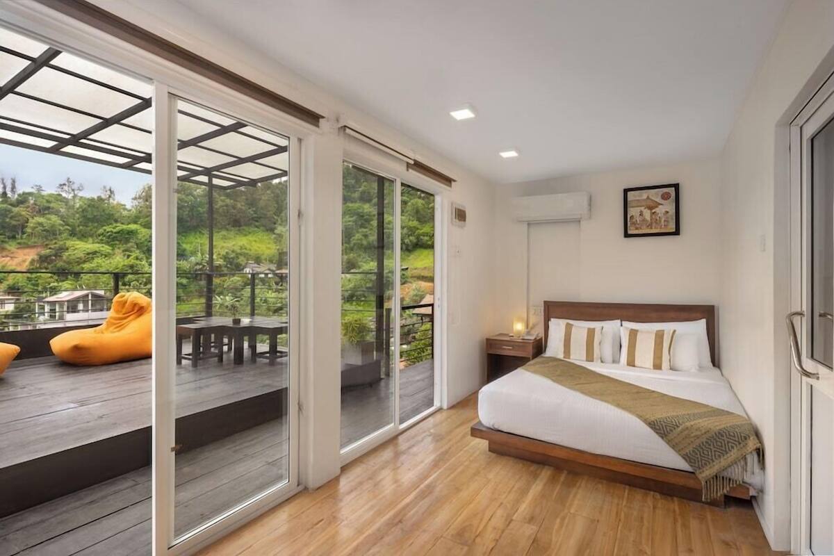 A bedroom with a large sliding glass door leading to an outdoor deck, a bed with a wooden headboard, and a small bedside table.