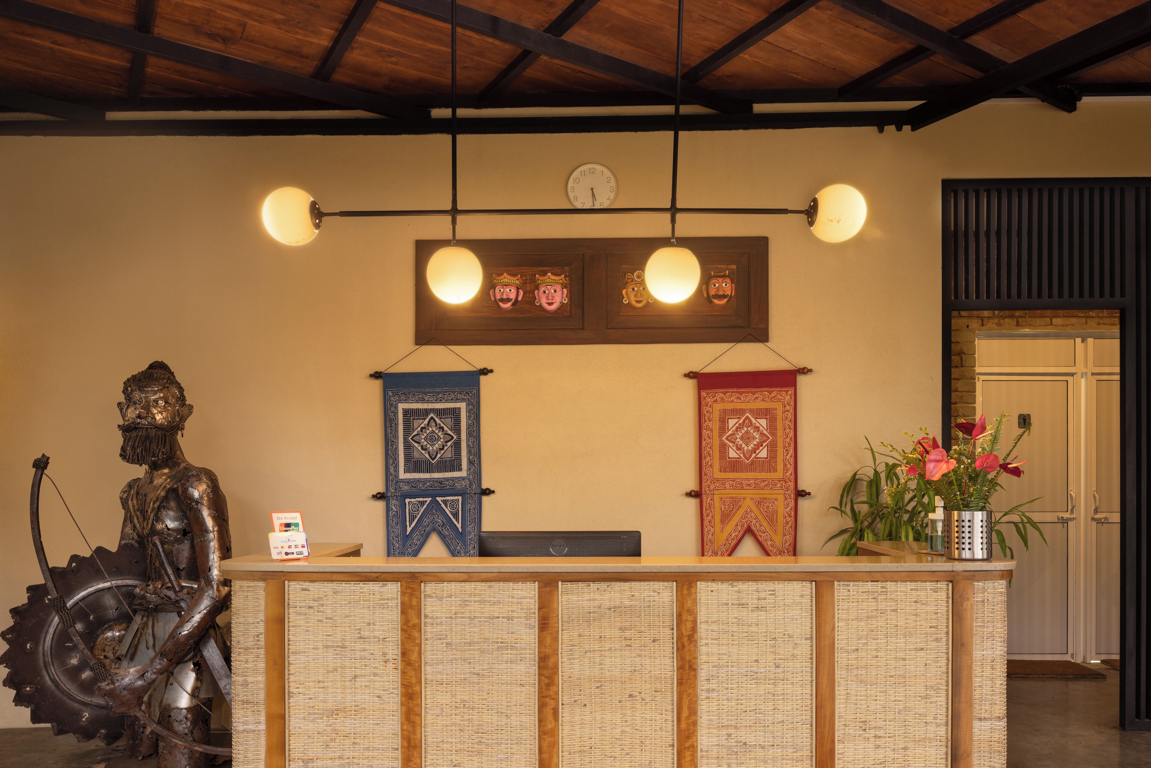 A reception desk with a clock, two framed masks, and a statue.