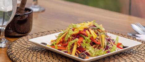 A table with a plate of colorful salad, a glass of water, and a small potted plant.