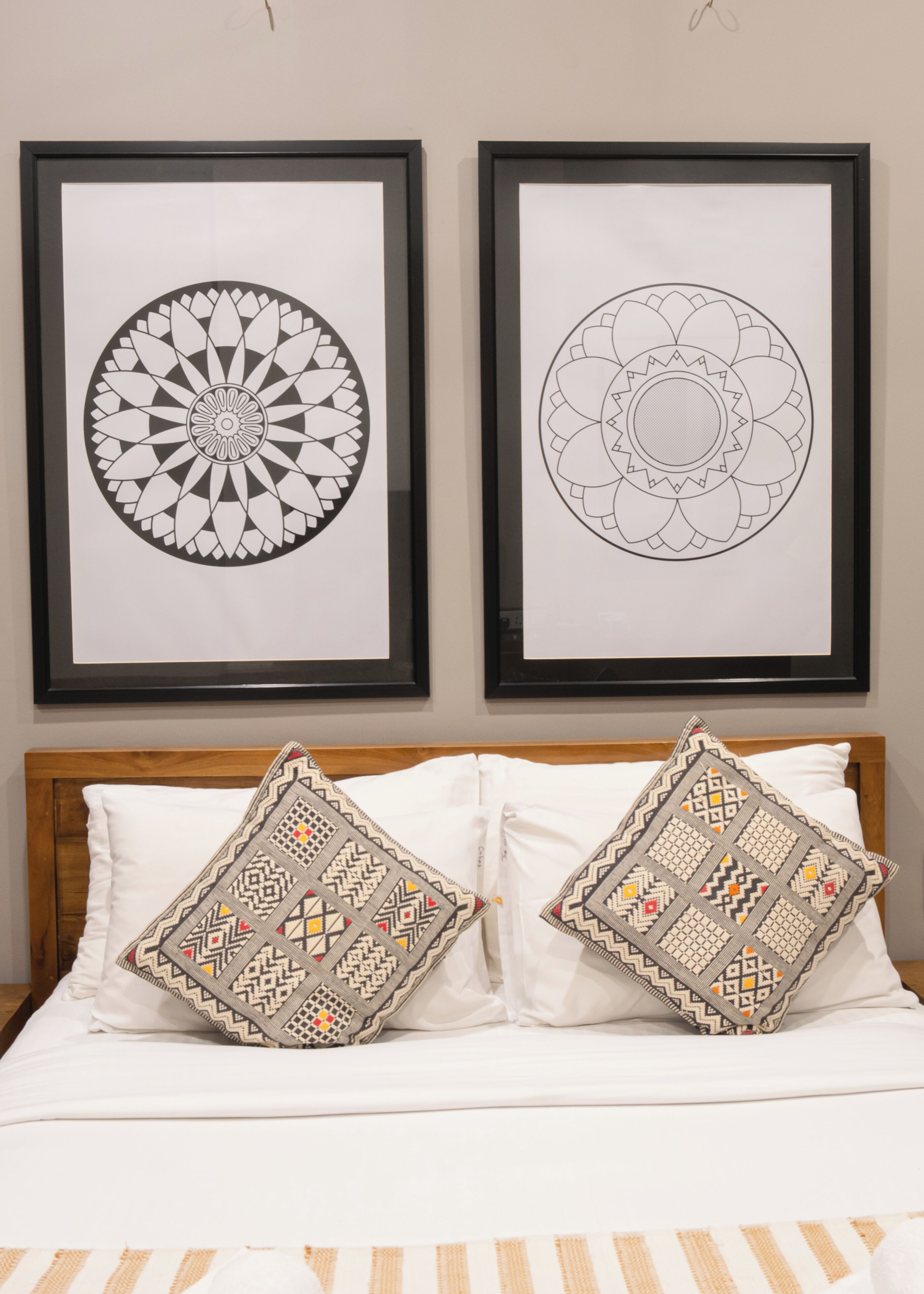 Dos diseños geométricos enmarcados en una pared sobre una cama con dos almohadas estampadas.