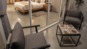 A modern living room with a large mirror reflecting a bedroom, a sofa, a coffee table, and a potted plant. - The Cubes Ella  (Ella)