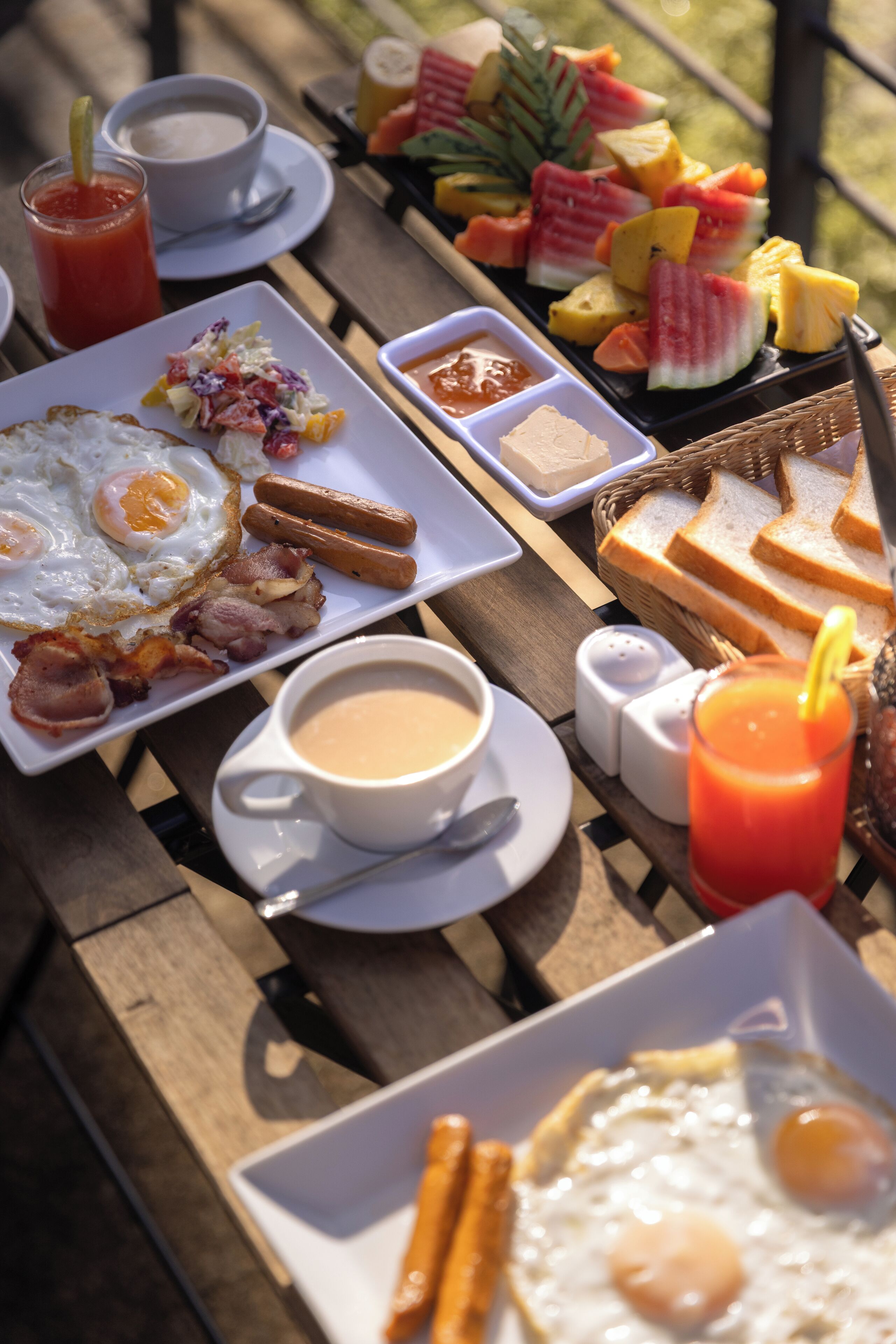 A breakfast spread on a wooden table including eggs, bacon, toast, and fruit.