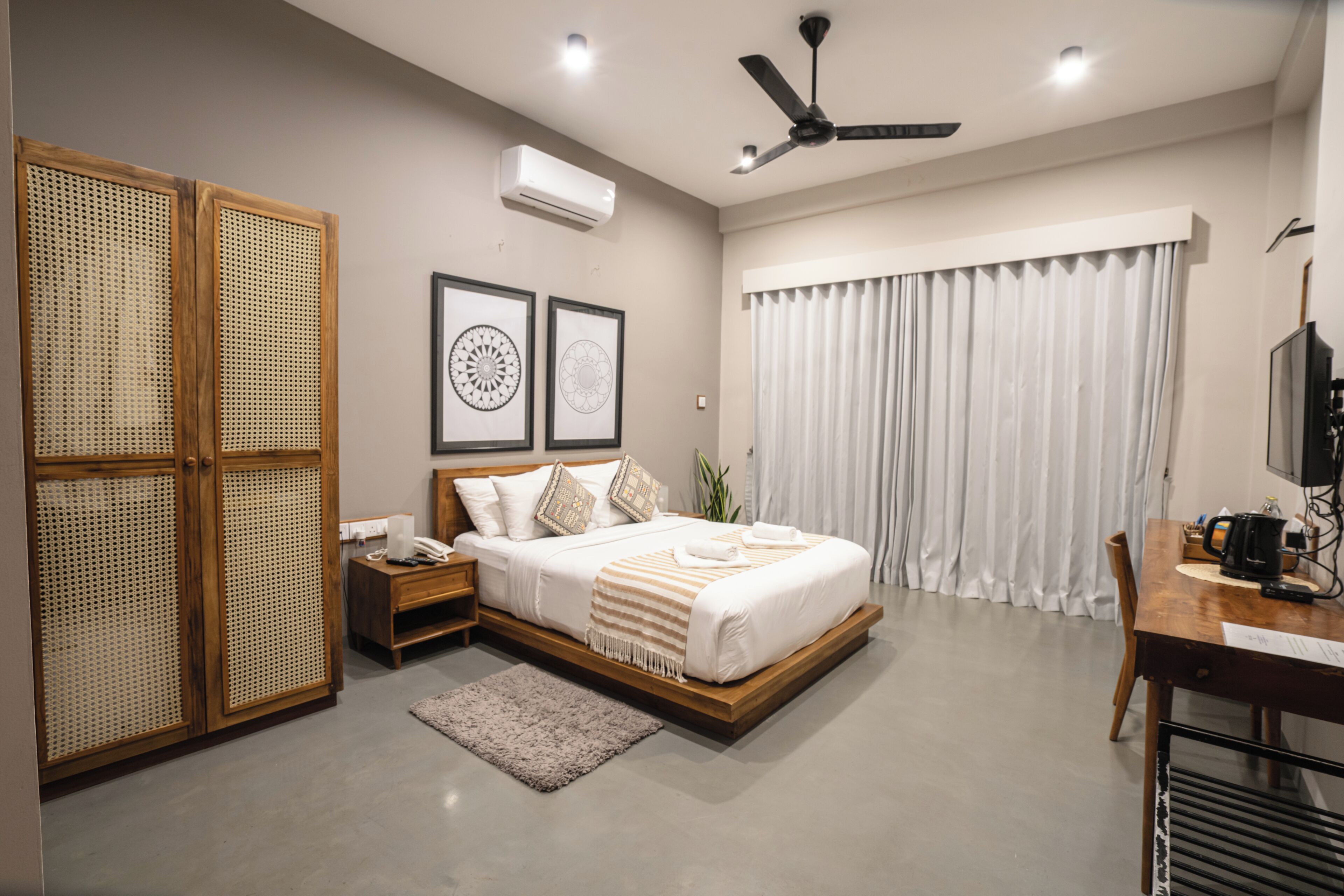 A bedroom with a bed, bedside tables, a desk, a ceiling fan, and a window with curtains.