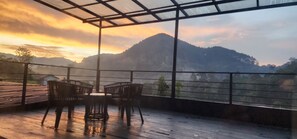 A covered outdoor seating area with a table and chairs, overlooking a mountainous landscape. - The Cubes Ella  (Ella)