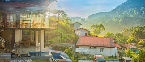A modern building with a glass facade, outdoor seating area, and a view of a hilly landscape.