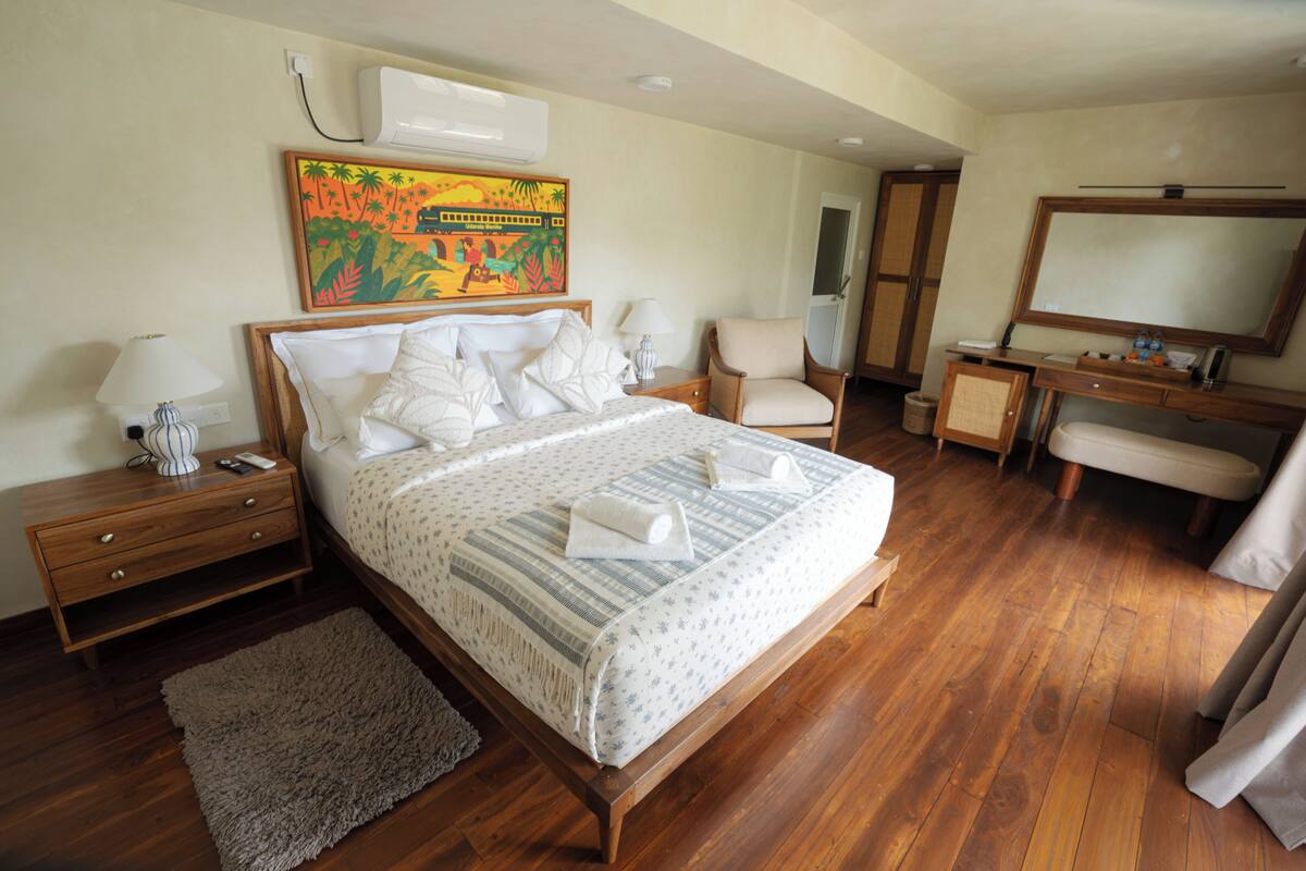A bedroom with a bed, bedside tables, a desk, a chair, a mirror, and a painting on the wall.