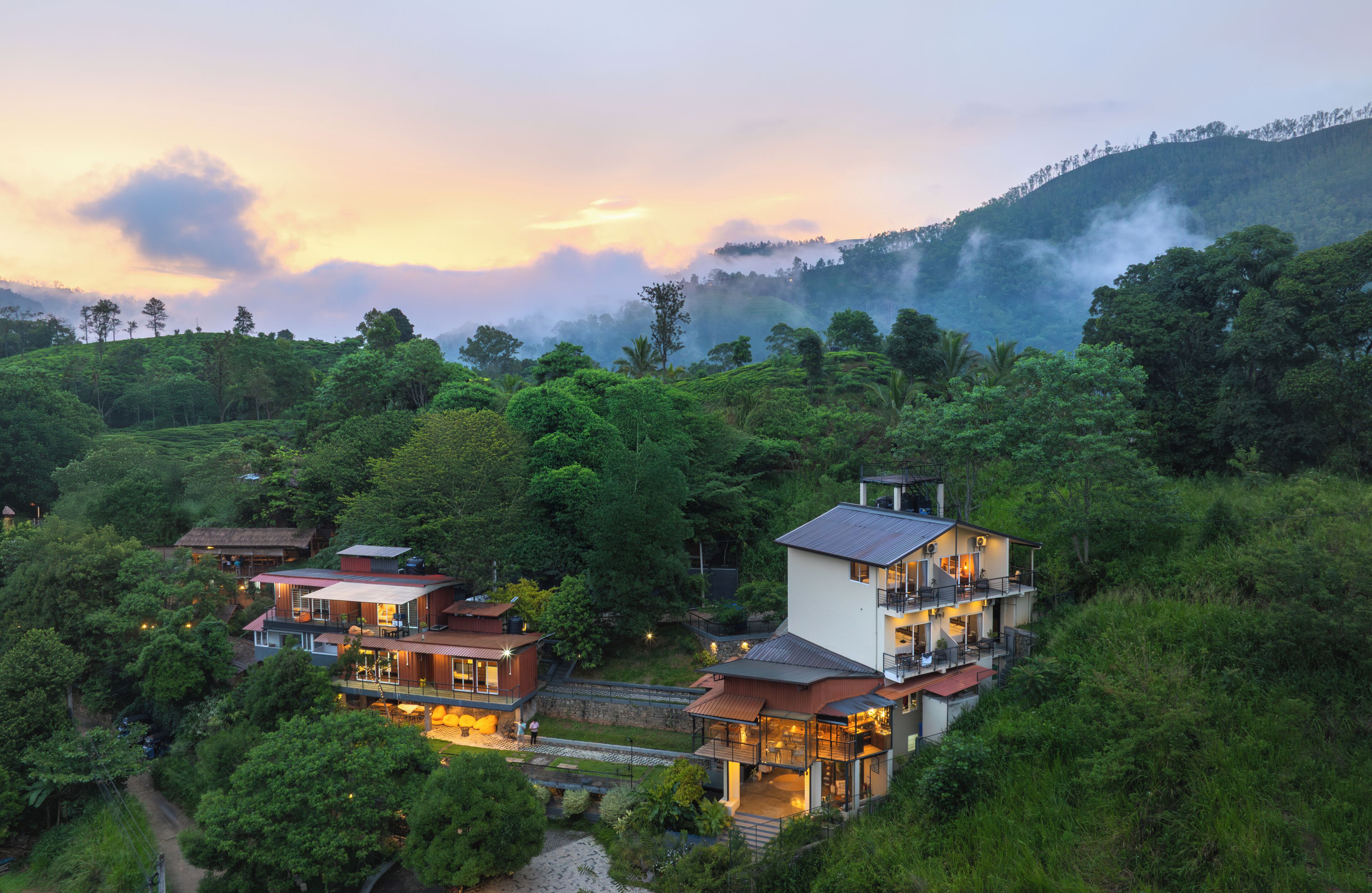 A hillside property with multiple houses, lush greenery, and a mountainous backdrop.