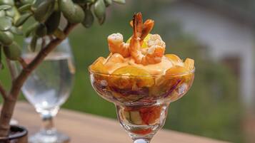 A dessert in a glass bowl on a woven placemat, with a potted plant and a wine glass in the background.