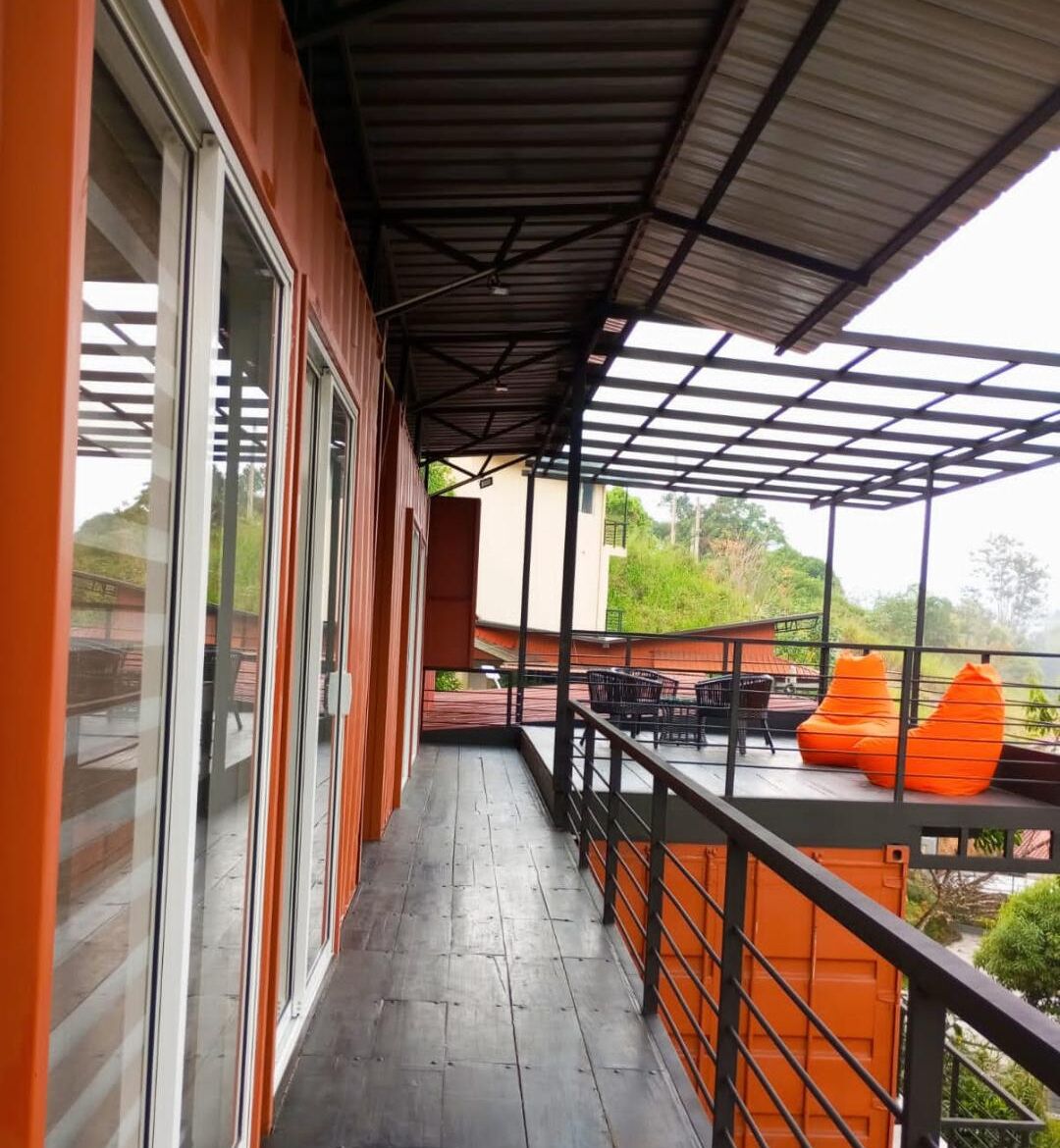 A covered balcony with a view of greenery, a table with chairs, and orange bean bag chairs.