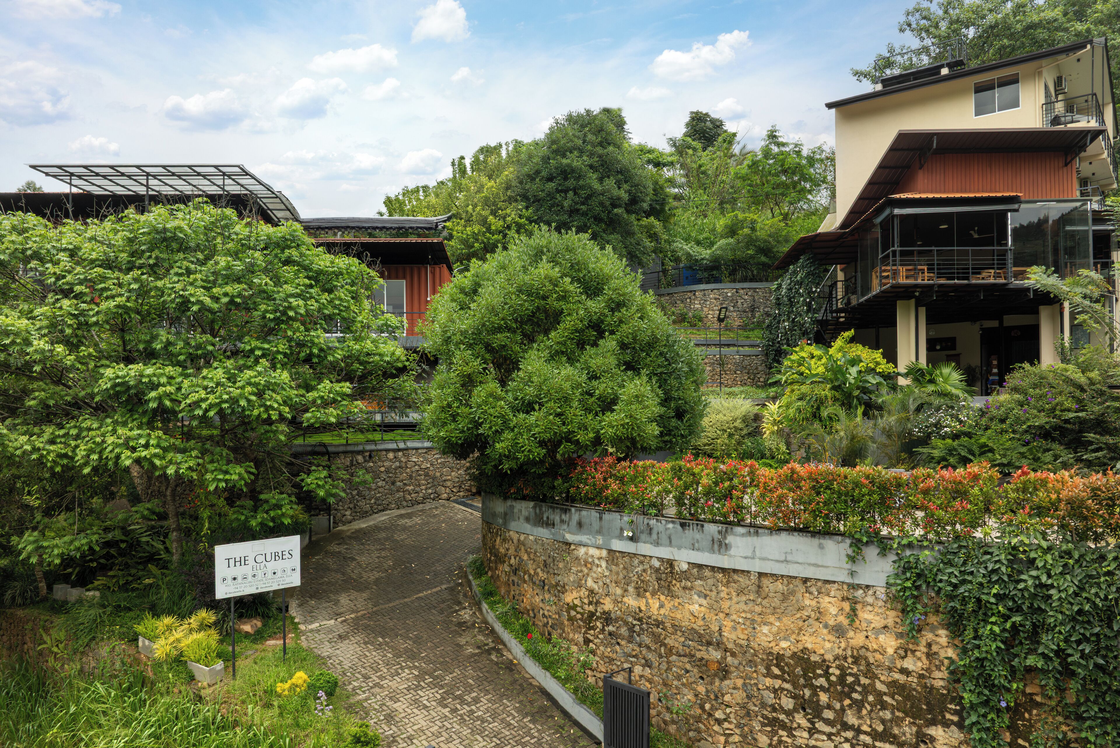 A residential area with a stone wall, a sign for 'The Cubes BIA', and lush greenery.