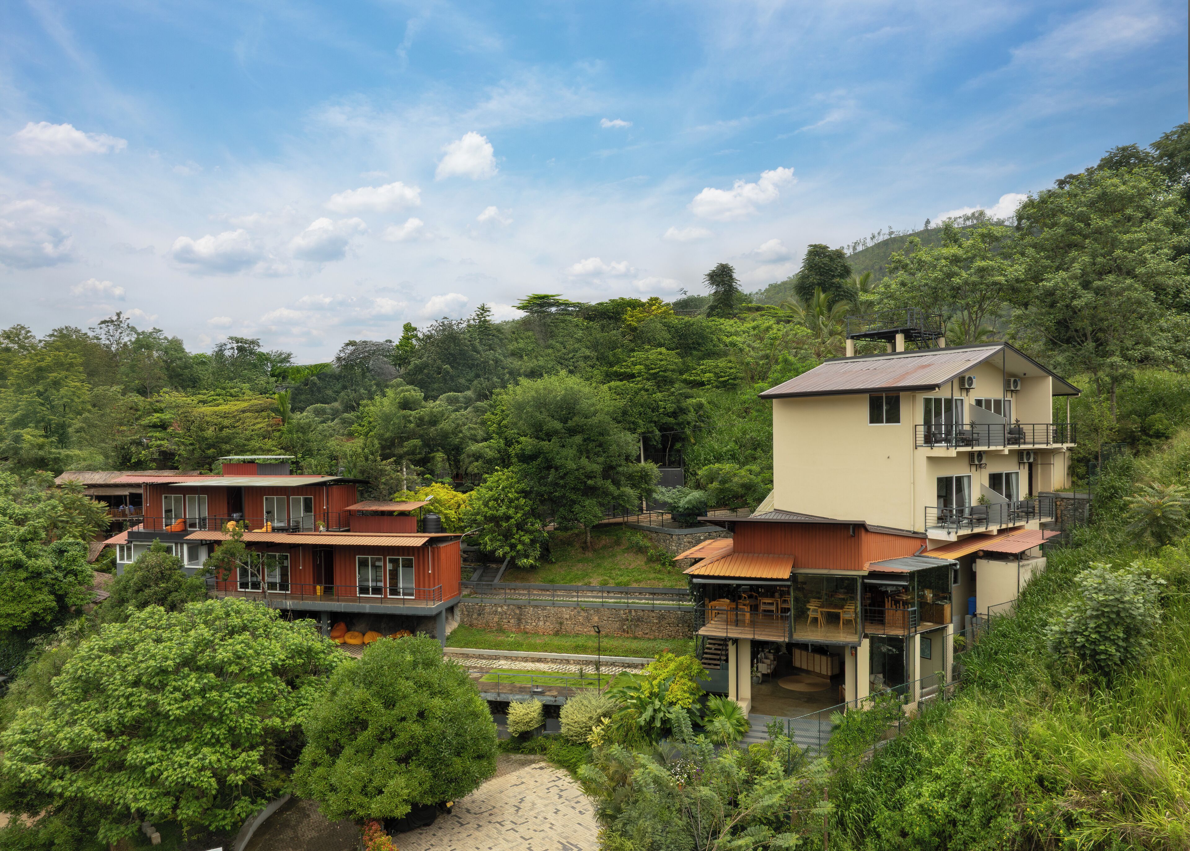 A hillside residential area with modern houses featuring balconies and large windows, surrounded by lush greenery and trees.