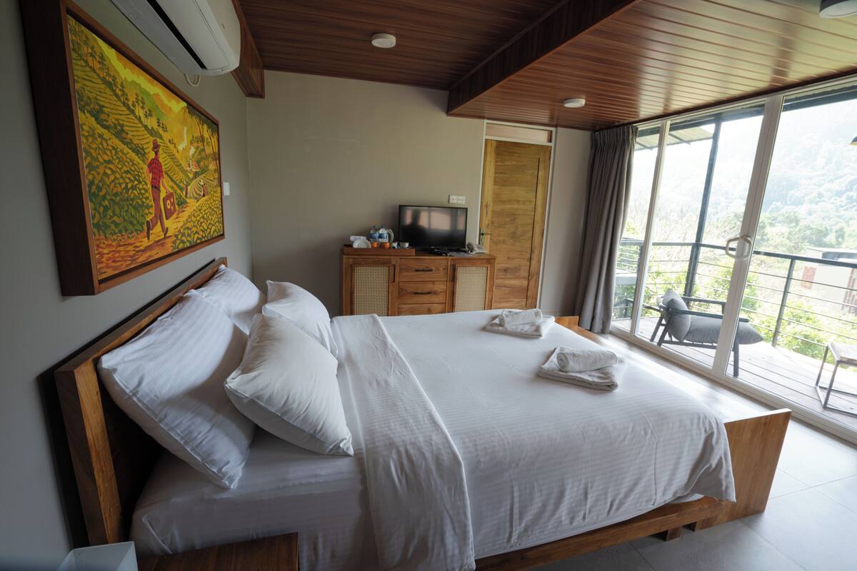 A bedroom with a large bed, a television on a wooden cabinet, and a painting on the wall.