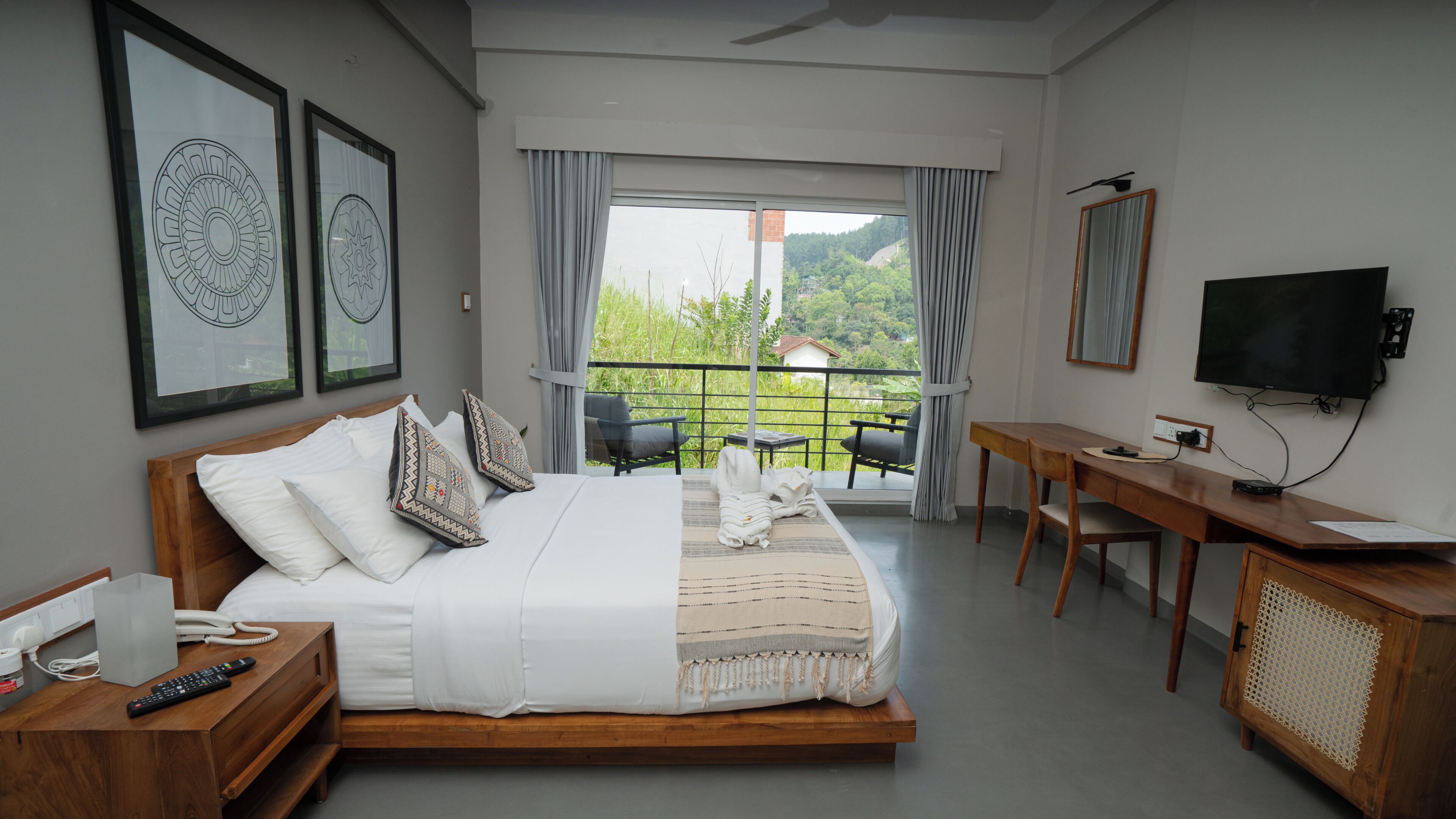 A bedroom with a bed, a desk, a TV, and a balcony with a view.