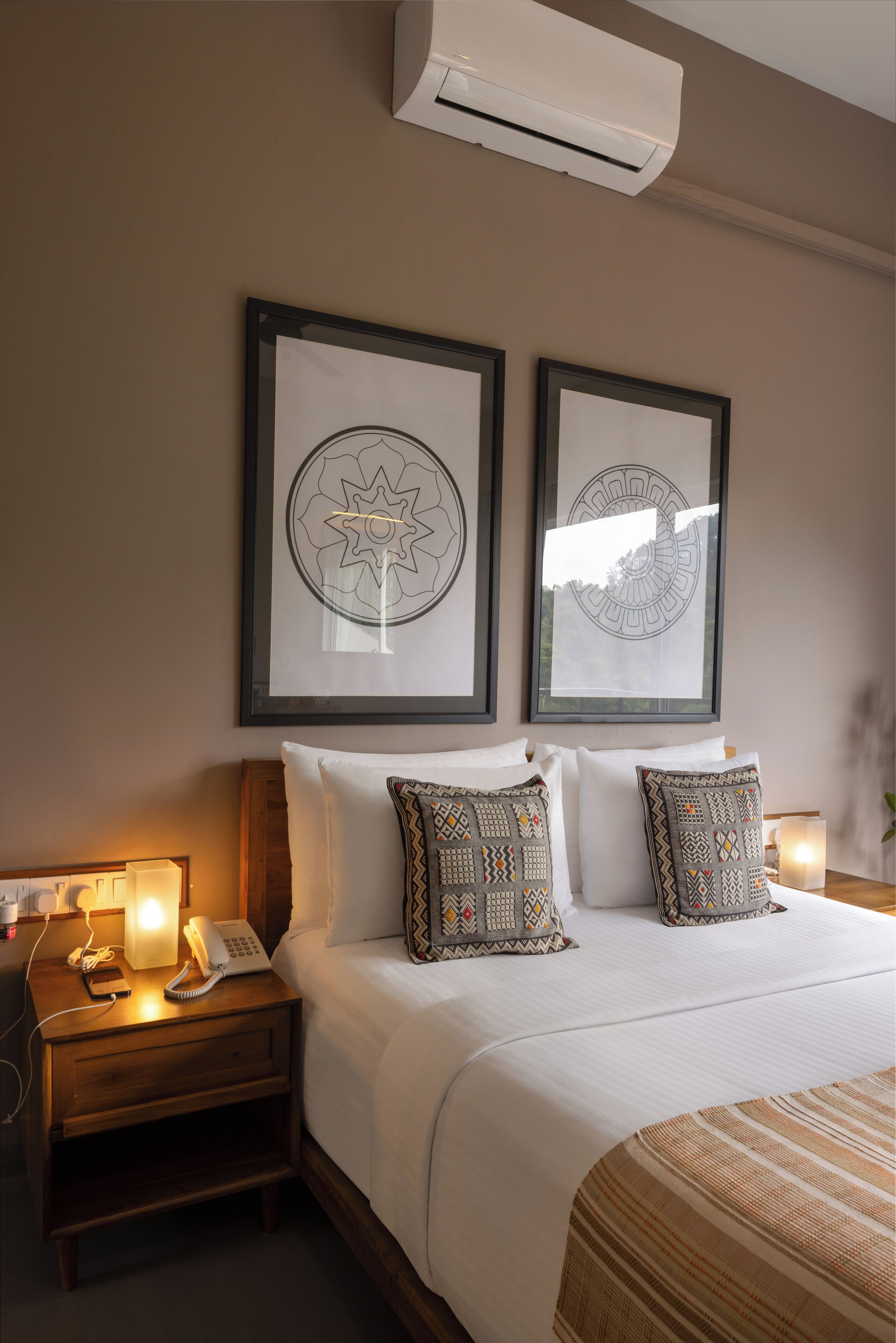 A neatly made bed with patterned pillows, a bedside table with a lamp and phone, and two framed wall art pieces.