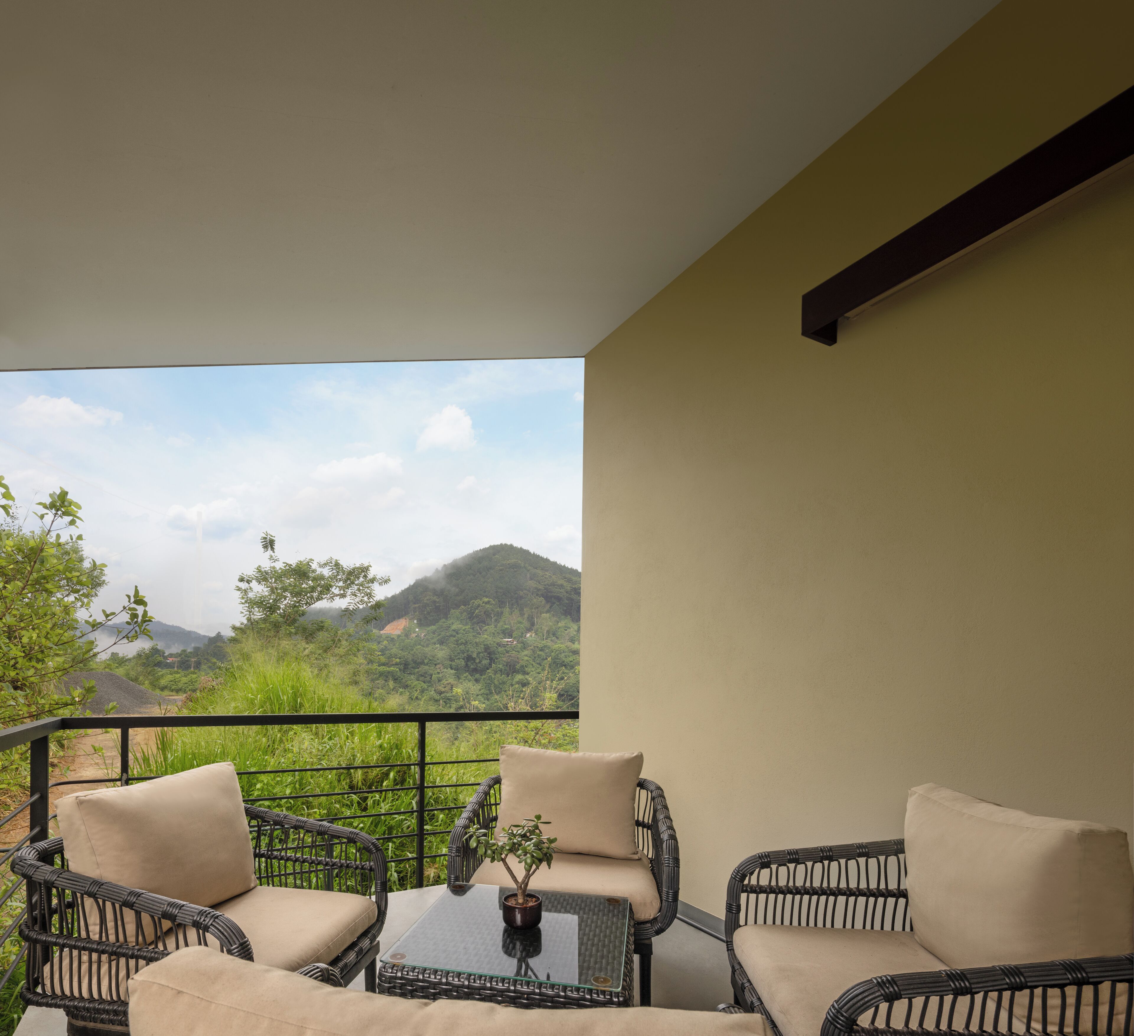 Ein Balkon mit Korbmöbeln und einem Tisch, mit Blick auf eine gebirgige Landschaft.