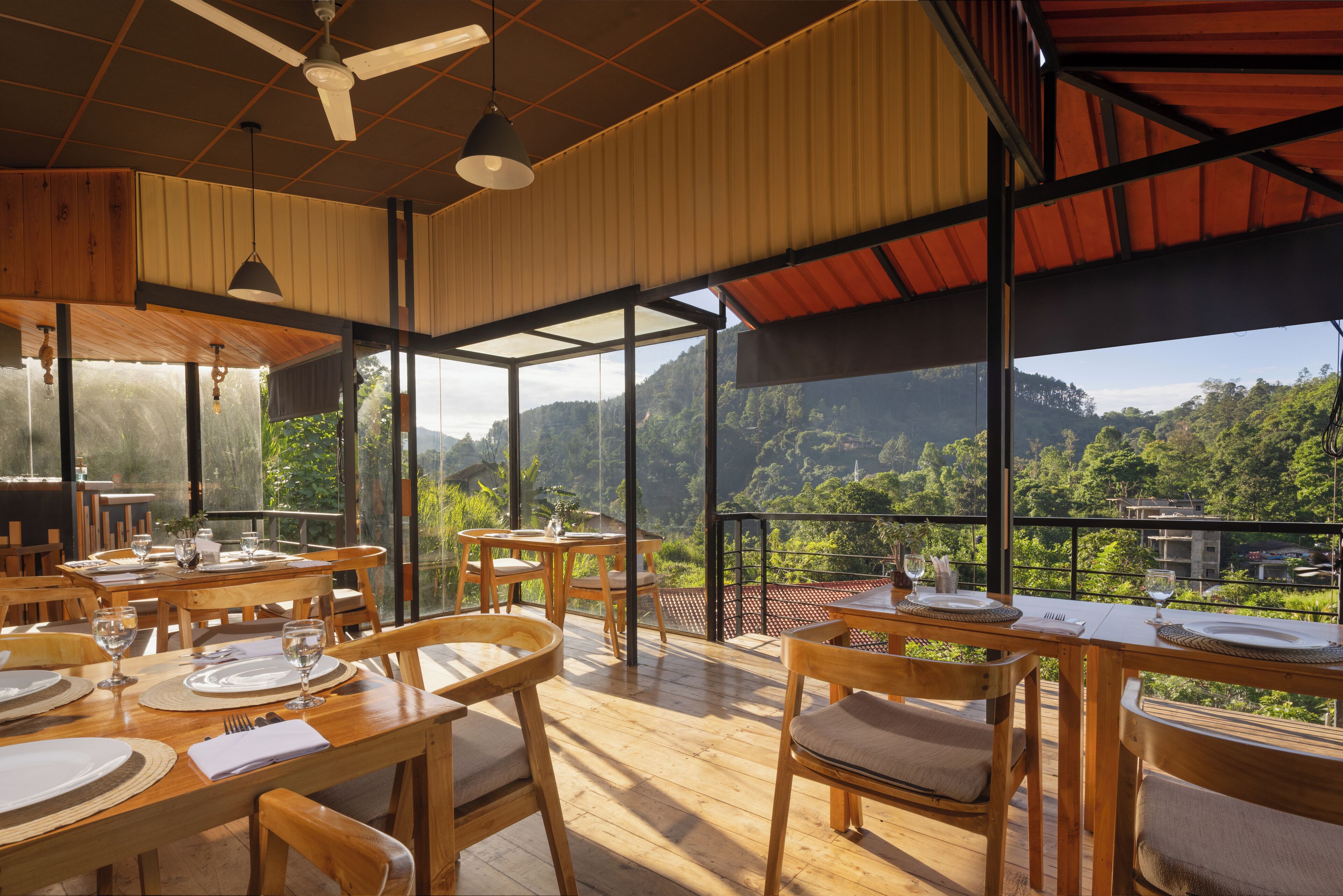 A restaurant with wooden tables and chairs, large windows, and a view of a mountainous landscape.