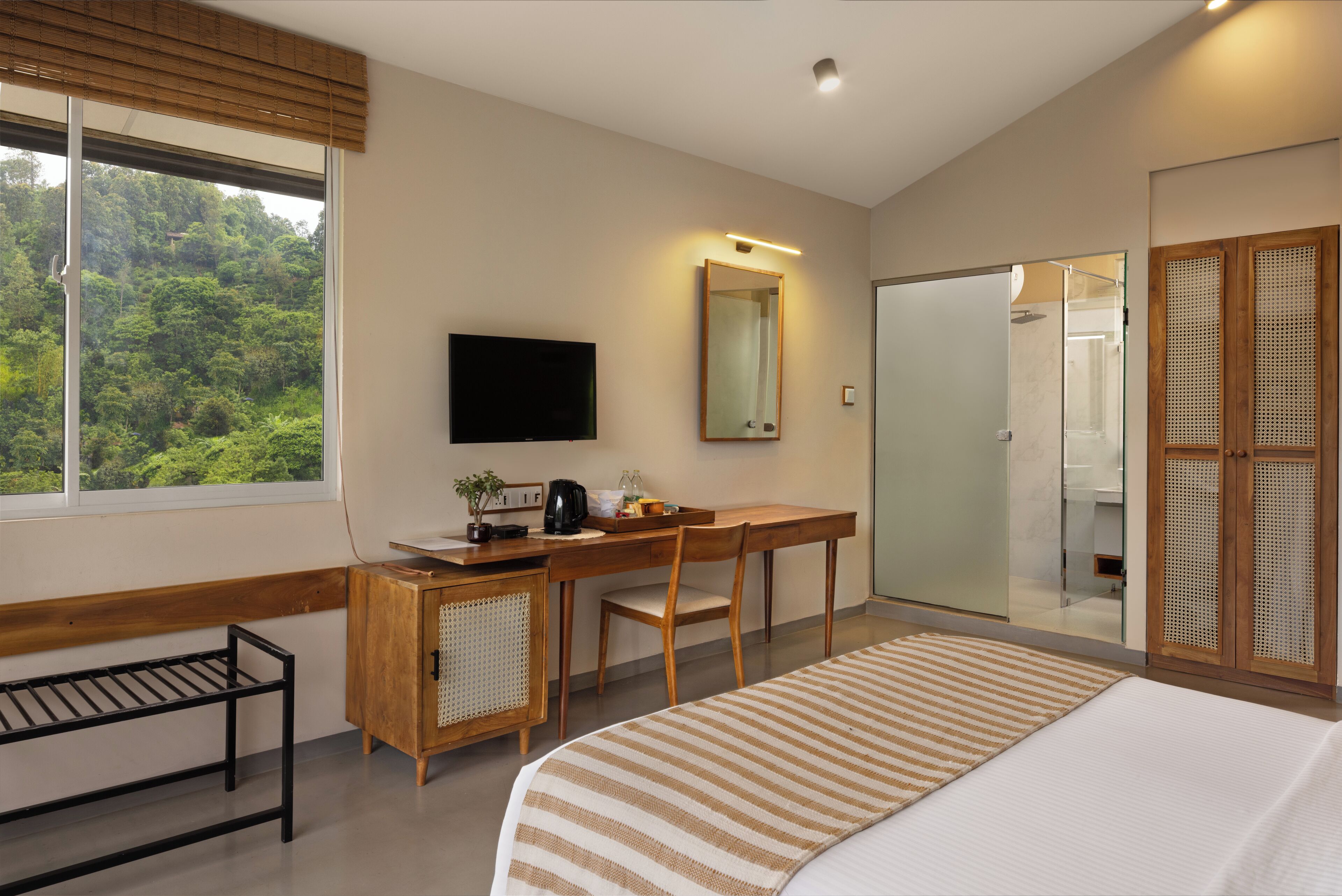 Un hotel moderno con una cama grande, un escritorio con una silla, un televisor, un espejo y vistas a un bosque por la ventana.