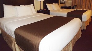 Habitación de hotel con dos camas, cada una con sábanas blancas y cabeceros marrones. Entre las camas, un mesita de noche con una lámpara.