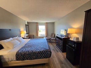 A hotel room with a large bed, a desk, a chair, a television, and a microwave.