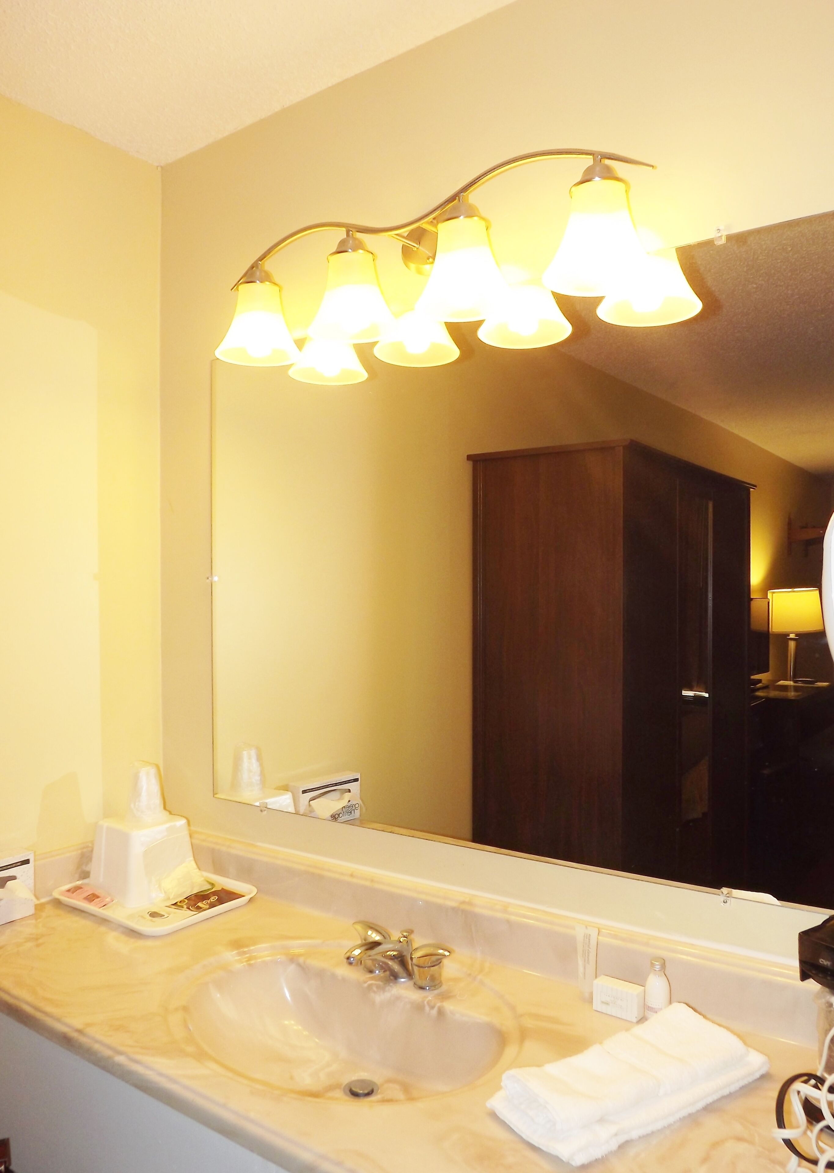 Une salle de bain d’hôtel avec un grand miroir, un lavabo et un espace coiffeuse.